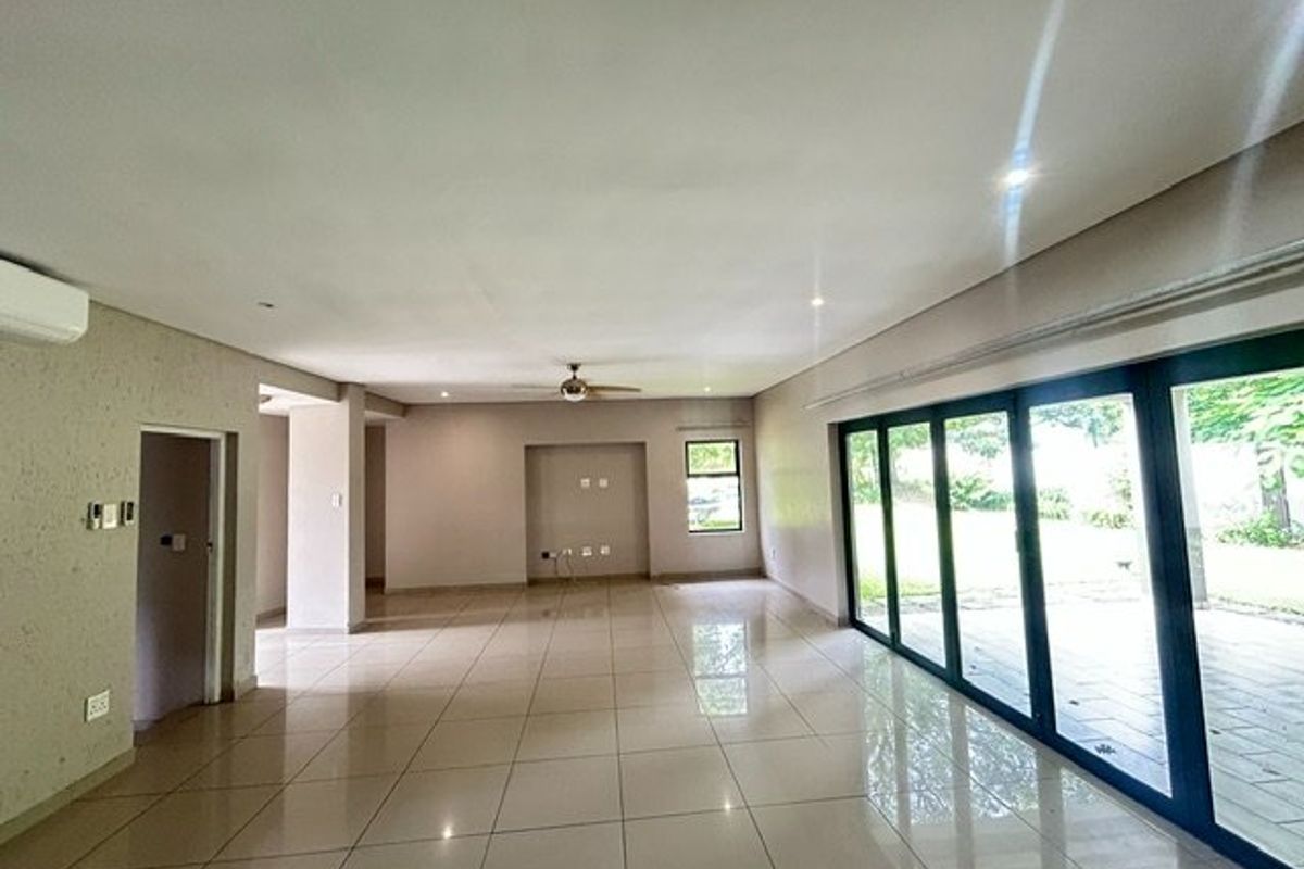 Spacious, light-filled open-plan living area featuring large aluminium stacker doors, neutral tiled flooring, and modern recessed lighting, offering seamless access to the outdoor patio.