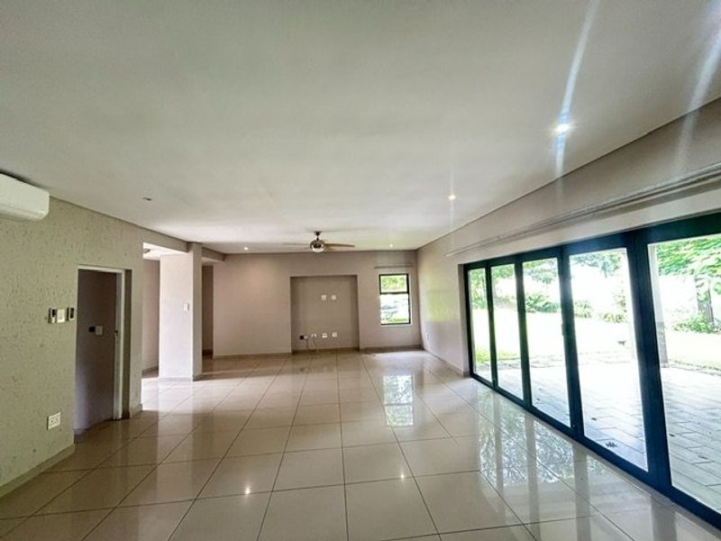 Spacious, light-filled open-plan living area featuring large aluminium stacker doors, neutral tiled flooring, and modern recessed lighting, offering seamless access to the outdoor patio.