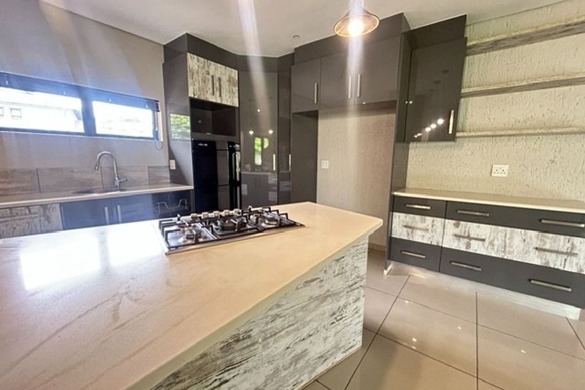 Modern kitchen featuring a central island with a gas hob, stone countertops, ample built-in cabinetry, and sleek tiled flooring.