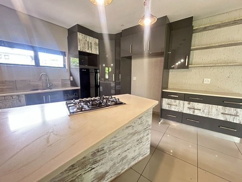 Modern kitchen featuring a central island with a gas hob, stone countertops, ample built-in cabinetry, and sleek tiled flooring.