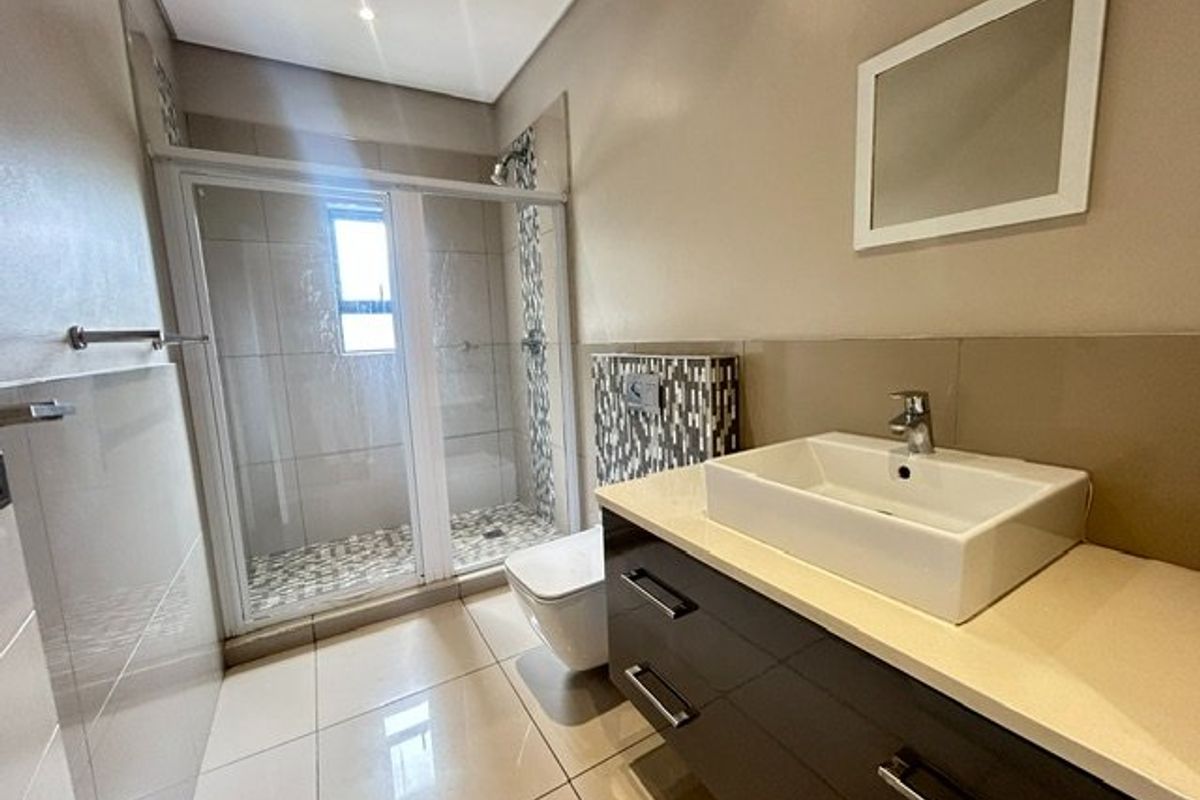Modern bathroom featuring a glass-enclosed shower, wall-mounted toilet, and a sleek vanity with a vessel sink and neutral tile finishes.