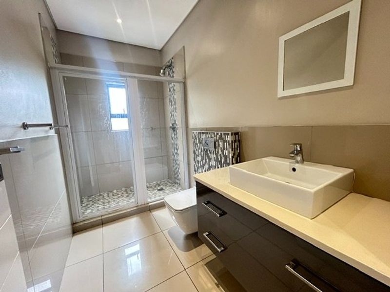 Modern bathroom featuring a glass-enclosed shower, wall-mounted toilet, and a sleek vanity with a vessel sink and neutral tile finishes.
