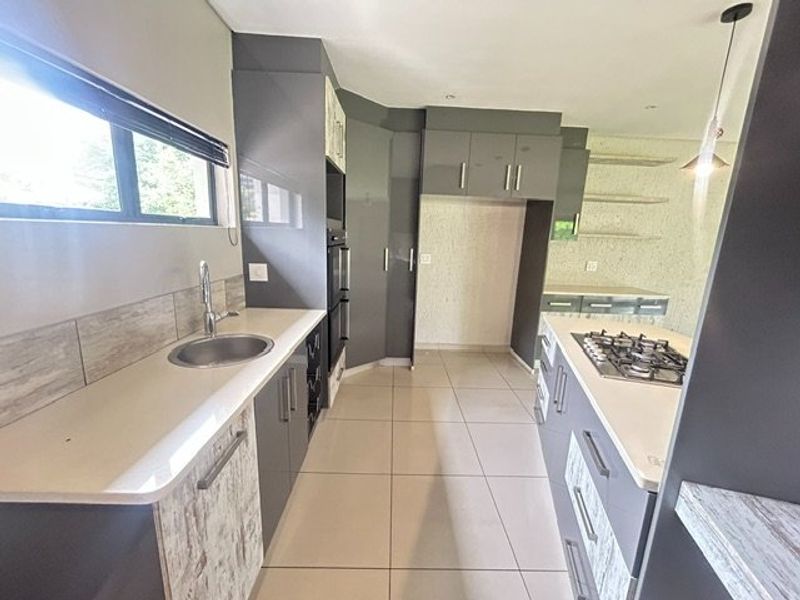 Modern kitchen featuring sleek grey cabinetry, stone countertops, a gas cooktop, built-in oven, and tiled flooring in a clean, open layout.