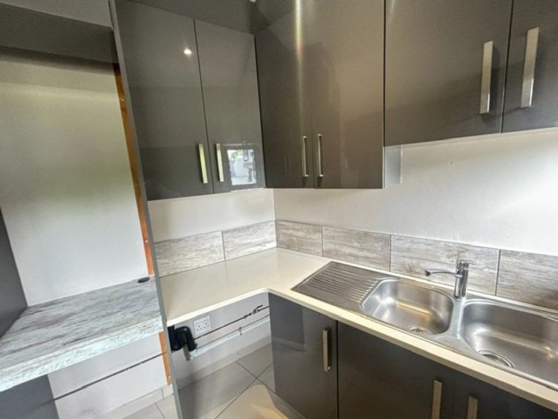 A modern scullery featuring glossy grey cabinetry, a stainless steel double sink, and stone-look tiled splashbacks, providing a functional secondary prep and wash-up area.