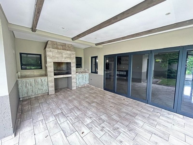 Covered patio featuring a built-in braai, tiled flooring, exposed ceiling beams, and large aluminium stacker doors providing seamless indoor-outdoor flow.