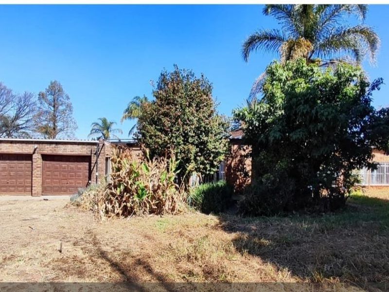 Front exterior view of a brick house featuring a double garage and established garden area requiring maintenance.