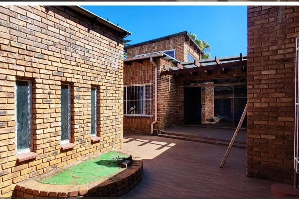 A private rear courtyard featuring face brick walls, paved flooring, and a timber pergola structure providing access to the main dwelling via sliding doors.
