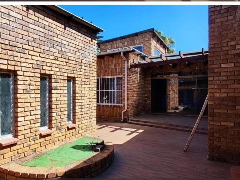 A private rear courtyard featuring face brick walls, paved flooring, and a timber pergola structure providing access to the main dwelling via sliding doors.