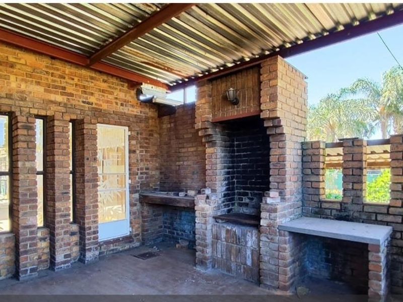 Covered outdoor patio featuring a built-in brick braai, concrete prep surfaces, and exposed brickwork, ideal for outdoor entertaining.