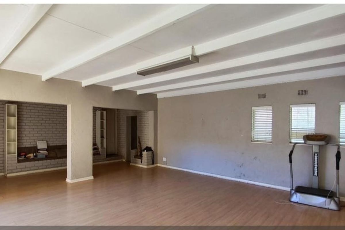 Spacious living area featuring exposed ceiling beams, laminate flooring, and built-in brick shelving, offering a versatile blank canvas for renovation.