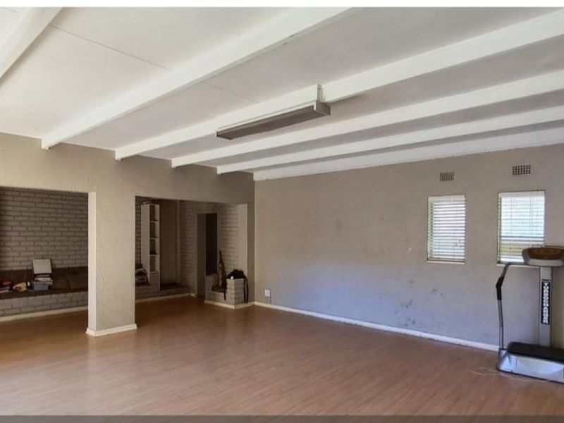 Spacious living area featuring exposed ceiling beams, laminate flooring, and built-in brick shelving, offering a versatile blank canvas for renovation.