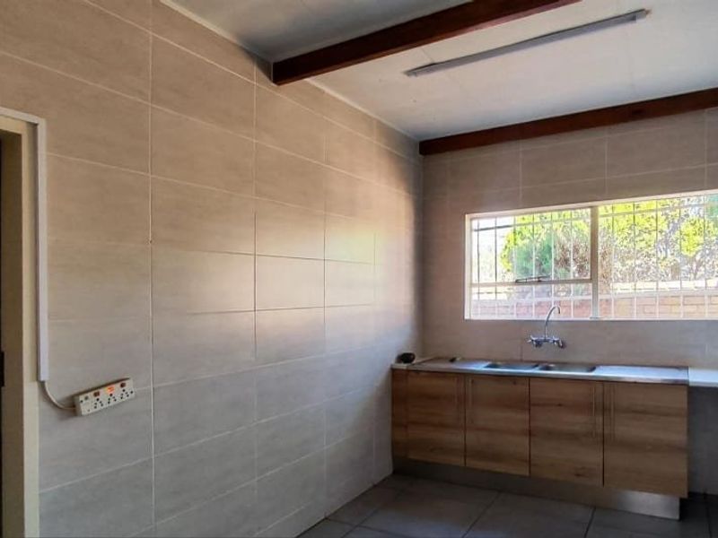 A functional scullery or utility area featuring tiled walls, built-in cabinetry with a stainless steel sink, and natural light through a window with security bars.