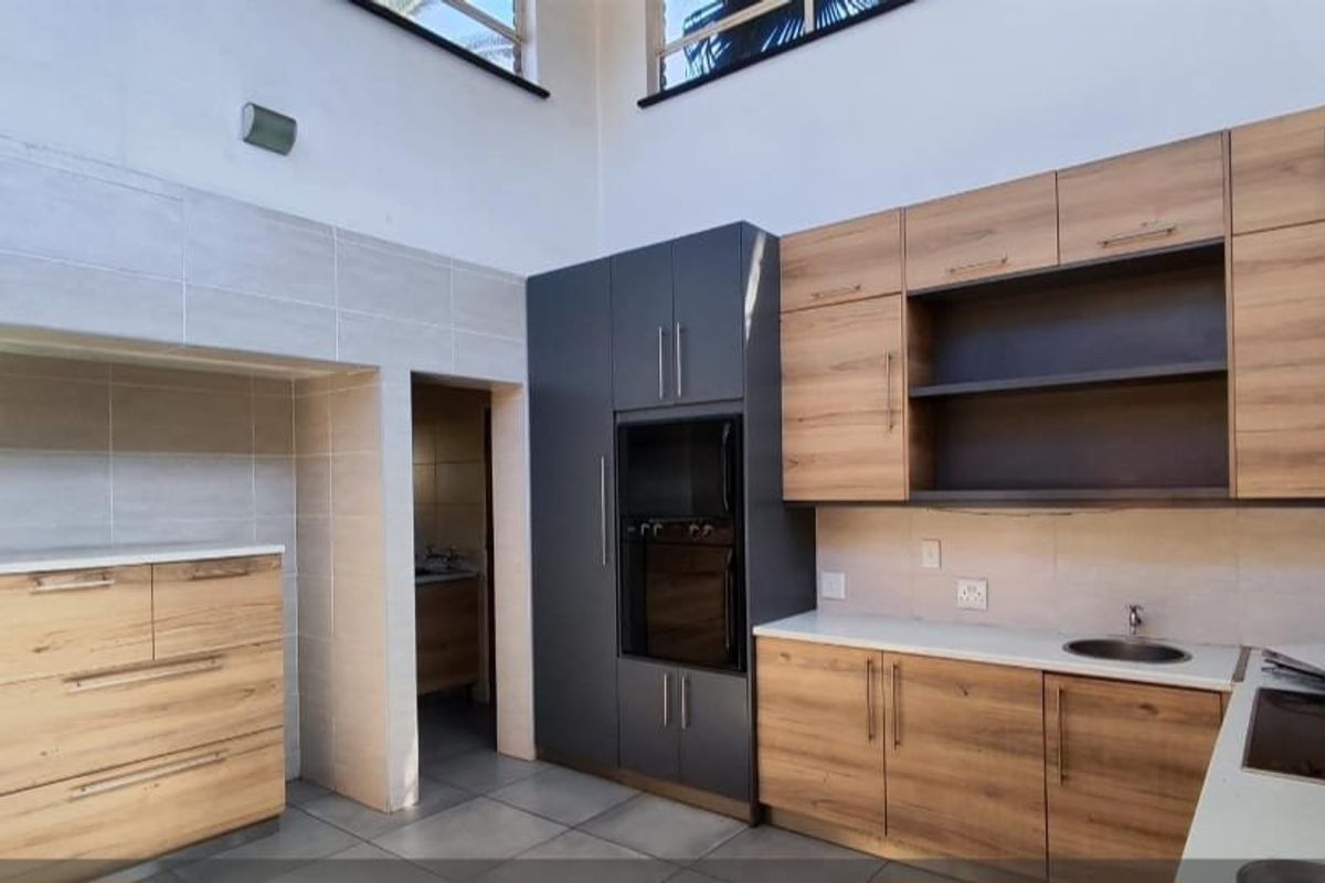 Modern kitchen featuring wood-grain cabinetry, dark grey pantry units, built-in oven, electric hob, and stone countertops with high ceilings.