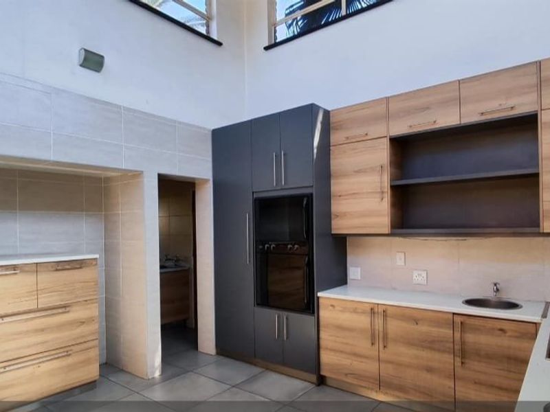 Modern kitchen featuring wood-grain cabinetry, dark grey pantry units, built-in oven, electric hob, and stone countertops with high ceilings.