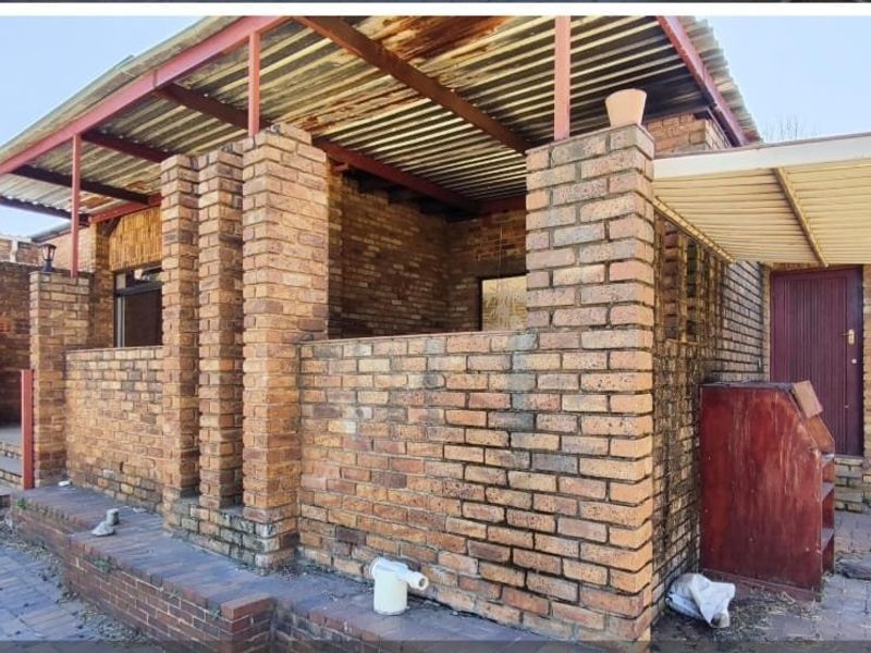 A rear exterior view of a face brick house featuring a covered patio area with corrugated metal roofing and paved outdoor space.