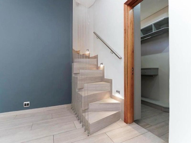 Modern hallway featuring a contemporary staircase with cable balustrade, recessed lighting, and tiled flooring, leading to an adjacent storage or utility area.