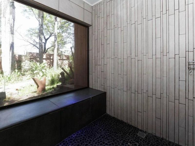 A modern bathroom featuring a unique pebble floor, textured wall tiling, and a large window overlooking the garden.