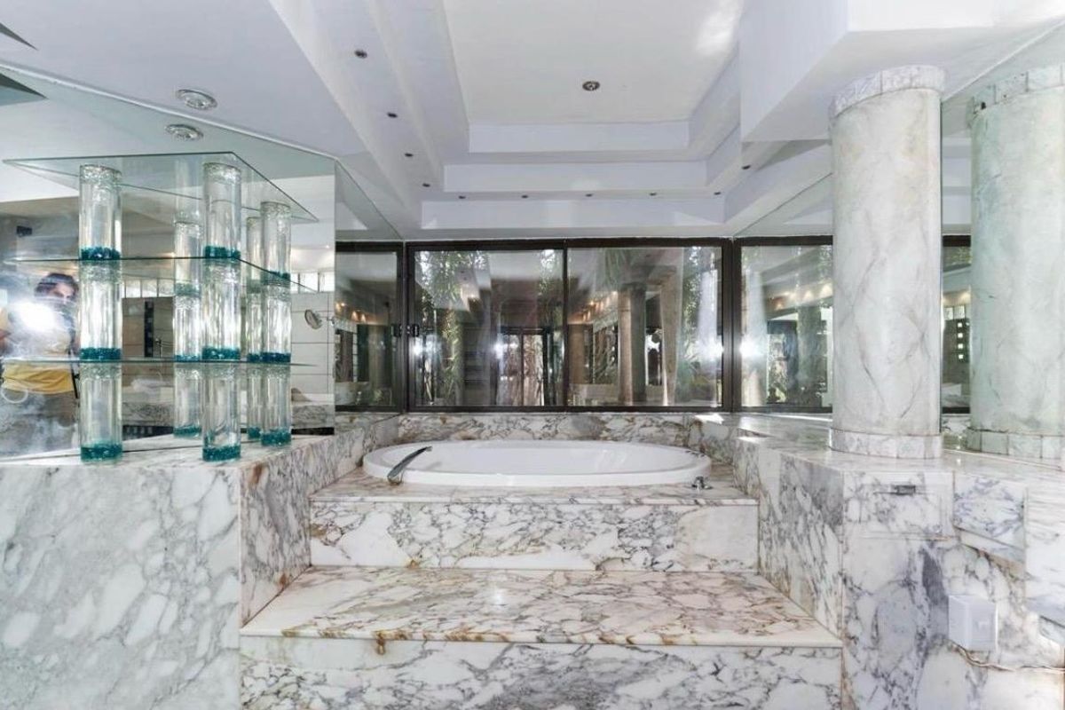 Luxurious bathroom featuring a raised built-in marble bathtub, marble wall finishes, recessed ceiling lighting, and large sliding glass doors.