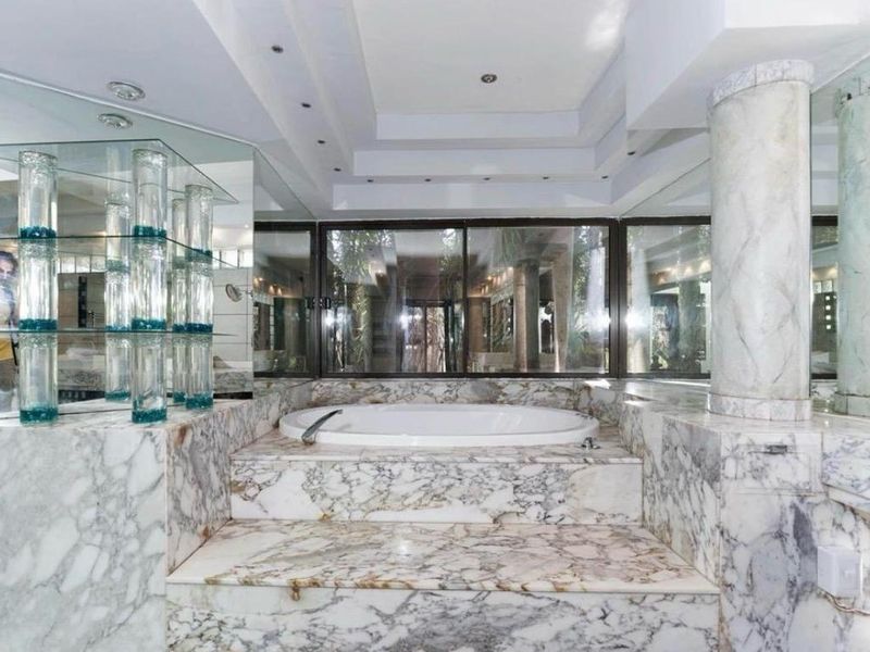 Luxurious bathroom featuring a raised built-in marble bathtub, marble wall finishes, recessed ceiling lighting, and large sliding glass doors.