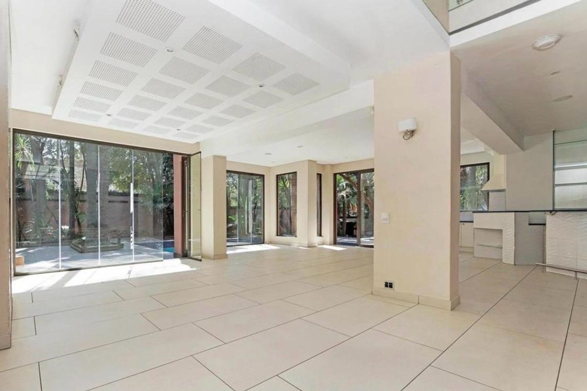 Spacious open-plan living area featuring large format floor tiles, recessed ceiling details, and expansive glass doors opening to the garden and pool area.
