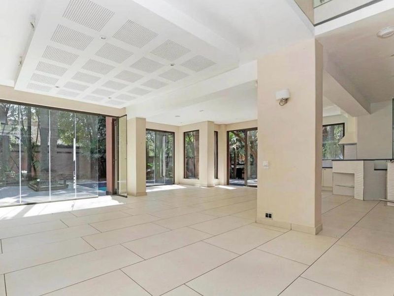 Spacious open-plan living area featuring large format floor tiles, recessed ceiling details, and expansive glass doors opening to the garden and pool area.