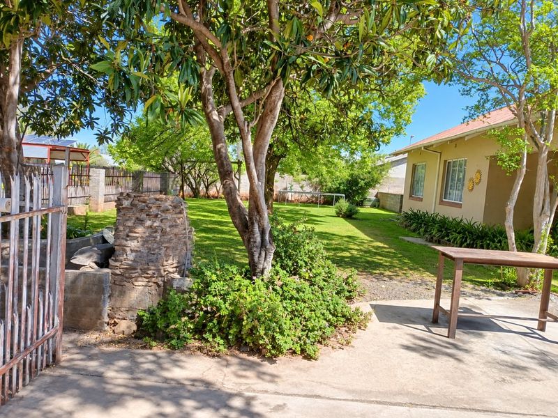 Spacious rear garden featuring a mature tree, stone-clad braai area, and concrete patio adjacent to the main house structure.