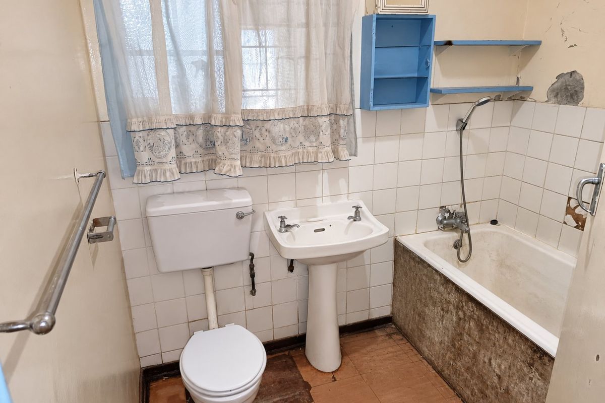A dated bathroom featuring a pedestal basin, toilet, and bathtub with handheld shower mixer, requiring significant renovation and cosmetic updates to improve condition.