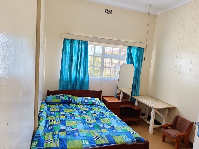 A bedroom featuring security bars on the window and visible water staining on the wall, requiring cosmetic attention.