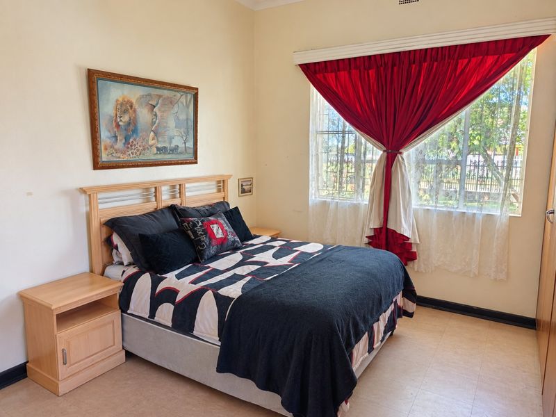 A functional bedroom featuring a window with security bars and built-in cupboard storage, offering a neutral base for potential interior updates.