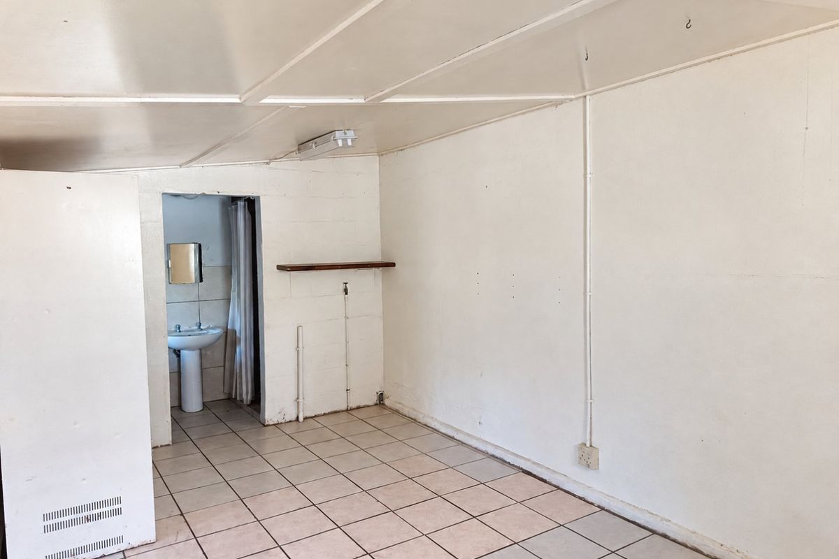 An empty bedroom featuring tiled flooring, exposed electrical conduit, and an attached en-suite bathroom with a pedestal basin.