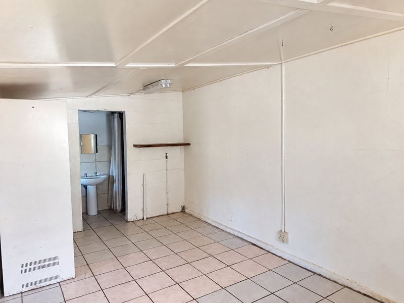 An empty bedroom featuring tiled flooring, exposed electrical conduit, and an attached en-suite bathroom with a pedestal basin.
