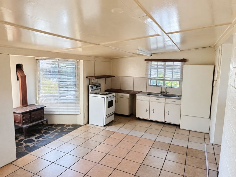 Open-plan kitchen and living area featuring a wood-burning stove, tiled flooring, and functional cabinetry, offering a blank canvas for renovation and modernization.