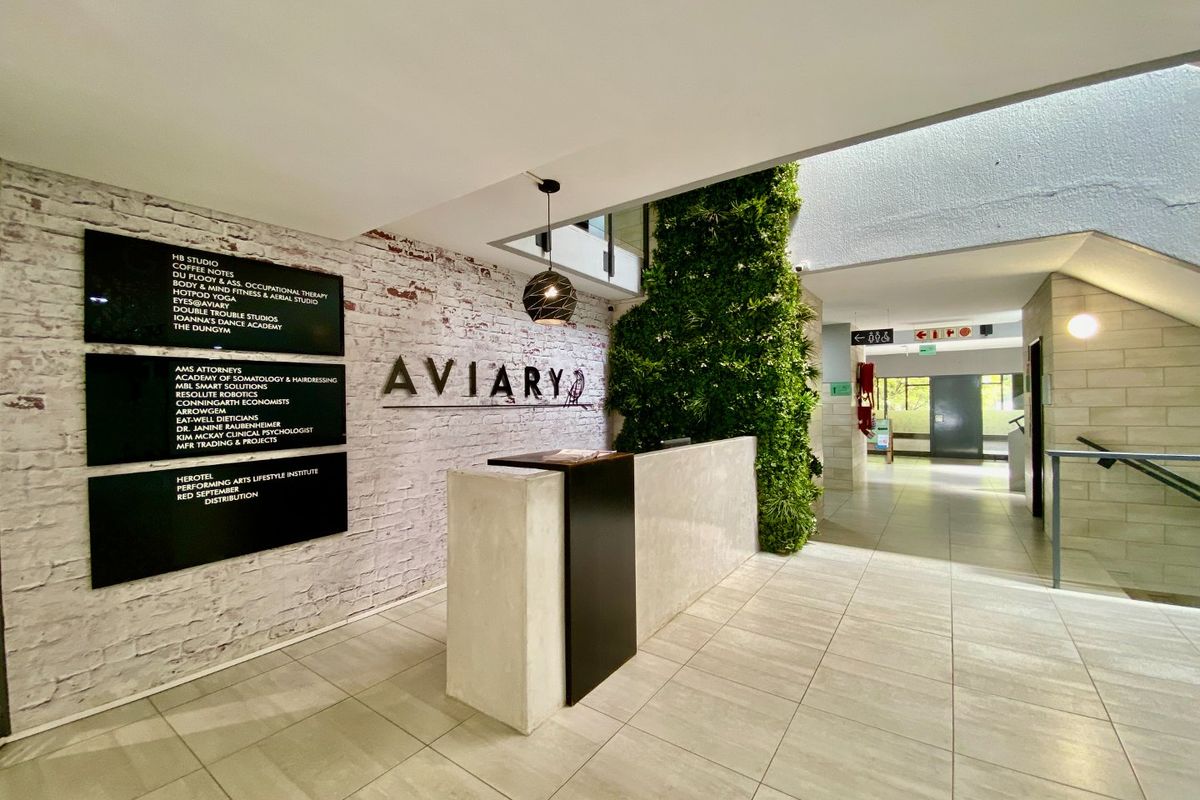 Modern commercial building entrance featuring a reception desk, directory signage, exposed brick wall, and a vibrant vertical garden feature.