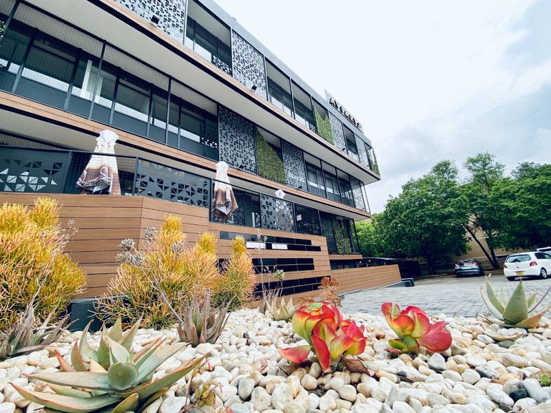 Modern commercial building facade featuring decorative metal screens, timber-look cladding, and a well-maintained landscaped rock garden in the foreground.