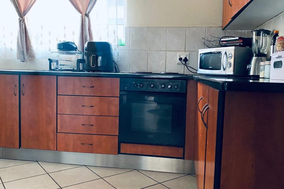 Functional kitchen featuring wood-finish cabinetry, dark stone countertops, built-in oven, electric hob, and tiled backsplash with ceramic floor tiles.