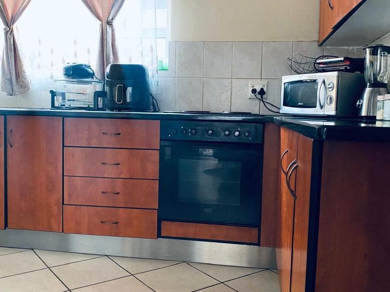 Functional kitchen featuring wood-finish cabinetry, dark stone countertops, built-in oven, electric hob, and tiled backsplash with ceramic floor tiles.