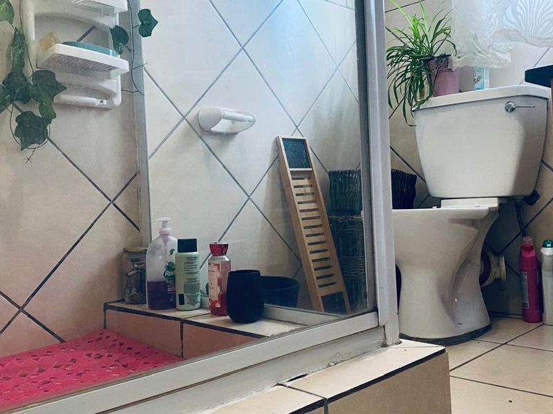 A functional bathroom featuring a shower enclosure and toilet with tiled finishes, currently showing signs of wear and requiring maintenance.
