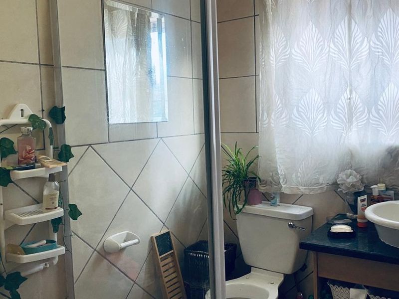 A functional bathroom featuring ceramic wall tiling, a vanity basin with a granite countertop, a toilet, and a shower enclosure.