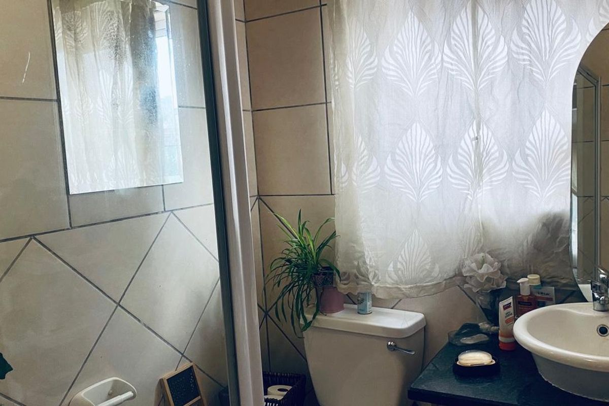 A functional bathroom featuring tiled walls, a vanity basin with mixer tap, and a shower enclosure.