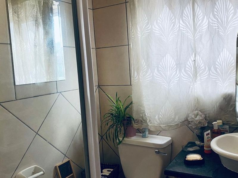 A functional bathroom featuring tiled walls, a vanity basin with mixer tap, and a shower enclosure.