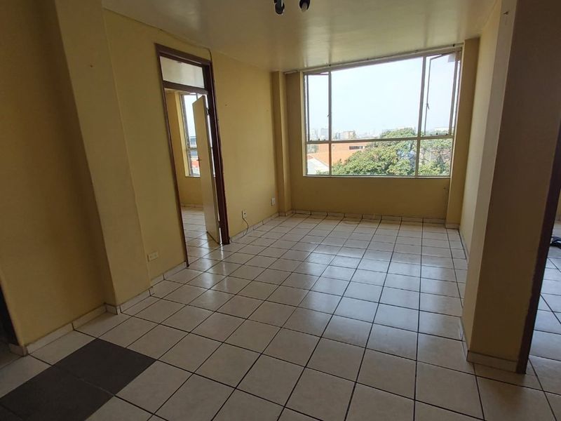 An empty living room featuring tiled flooring, large windows with natural light, and neutral wall finishes, ready for personalization.