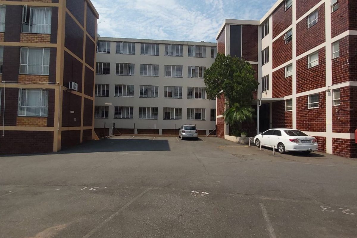 Exterior view of the apartment complex showing the rear parking area and multi-story brick building facades.