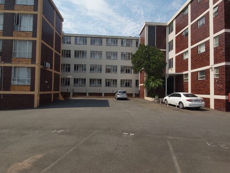 Exterior view of the apartment complex showing the rear parking area and multi-story brick building facades.