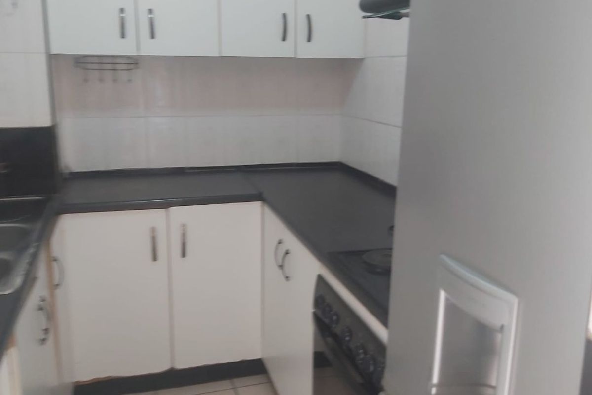 A compact kitchen featuring white cabinetry, dark countertops, built-in oven, and tiled flooring, offering a functional layout for daily meal preparation.