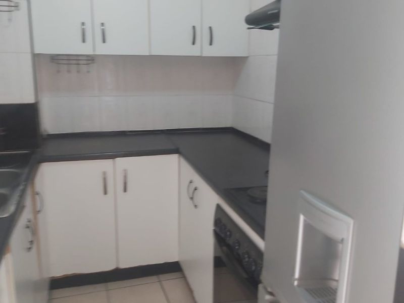 A compact kitchen featuring white cabinetry, dark countertops, built-in oven, and tiled flooring, offering a functional layout for daily meal preparation.