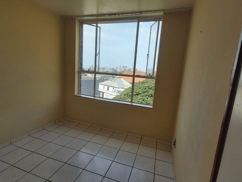 An empty bedroom featuring tiled flooring and a large casement window with an urban view.