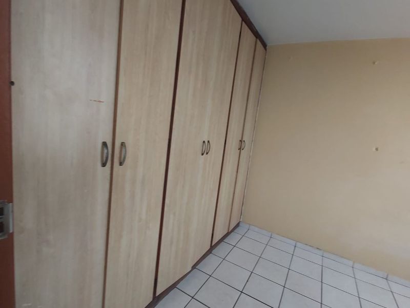 A vacant bedroom featuring light wood-finish built-in cupboards and neutral tiled flooring, offering a clean canvas for personalization.