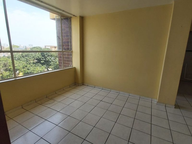 An empty living room featuring large windows with natural light and tiled flooring, offering a blank canvas for renovation and interior design.