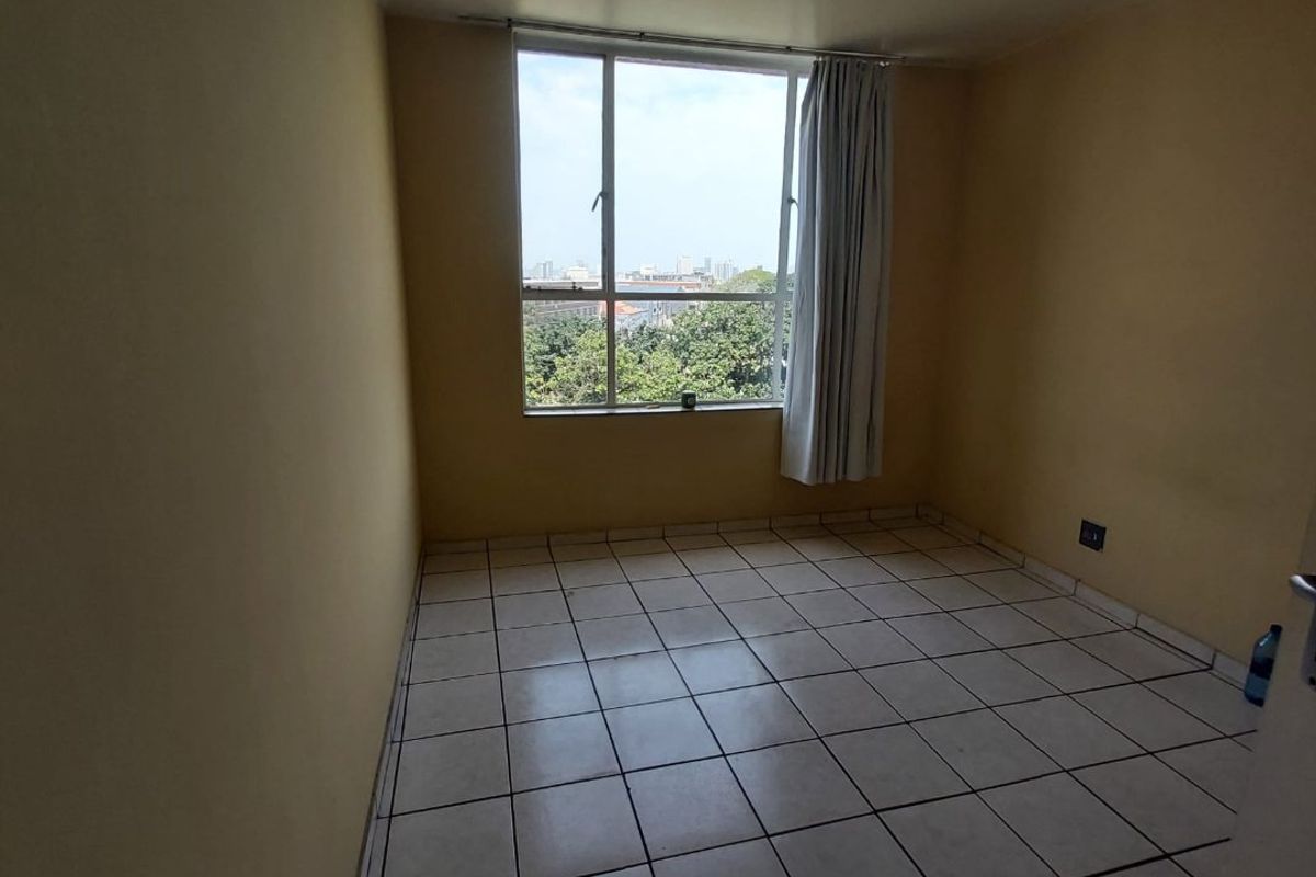 An empty bedroom featuring tiled flooring, neutral wall paint, and a large window providing natural light and an urban view.