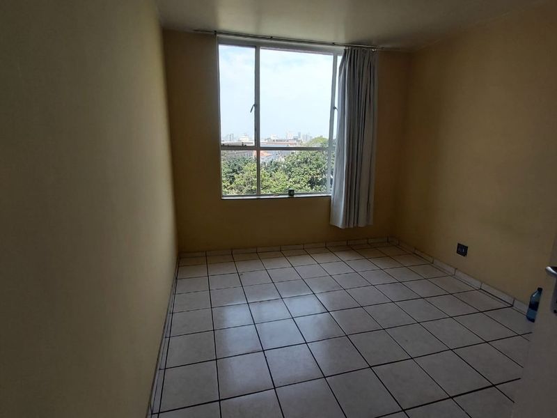 An empty bedroom featuring tiled flooring, neutral wall paint, and a large window providing natural light and an urban view.